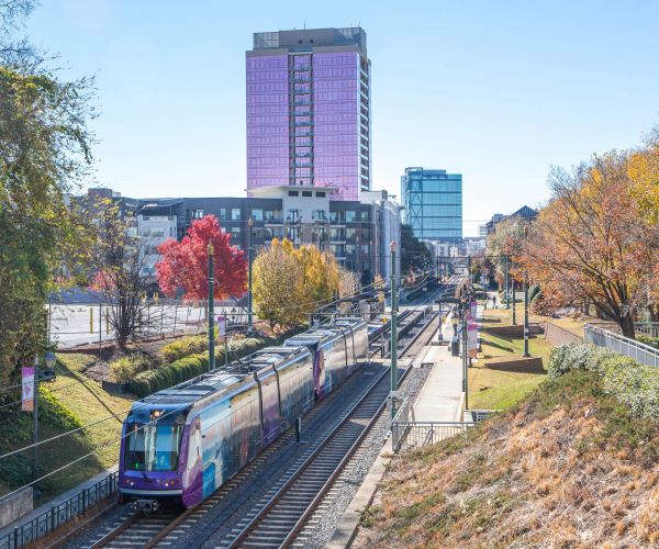 The Sloan at LoSo Apartments in Charlotte, NC, neighborhood area public transportation train with the city skyline in the background